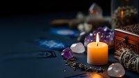 Mystical fortune telling setup with burning candle, crystal gems, tarot cards and ornate jewelry box creating atmospheric spiritual divination scene.
