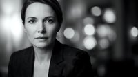 Professional middle-aged Caucasian businesswoman in formal suit with confident expression against blurred city lights background in black and white.