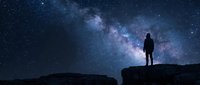 Person silhouette standing on rocky cliff under spectacular Milky Way galaxy with countless stars in deep blue night sky for astronomy and adventure themes.