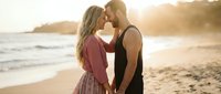 Young Caucasian couple sharing intimate moment on beach at golden hour sunset, romantic vacation getaway for wedding anniversary or honeymoon celebration.