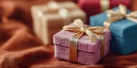 Colorful gift boxes with golden ribbons arranged on warm fabric surface for holiday celebrations and special occasions.