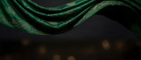 Elegant green silk fabric with golden accents flowing gracefully against dark background with warm bokeh lights for luxury design projects.
