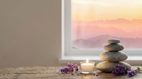 Zen spa stones balanced with lavender flowers and candle on wooden surface near window with sunset mountain view for meditation and wellness relaxation.