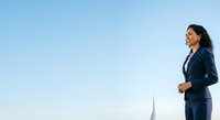 Young South Asian woman in professional navy blazer standing outdoors against clear sky, looking upward with confidence. Suitable for business, corporate, leadership, and career-related projects.