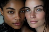 Close-up portrait of two diverse young women with natural makeup and glowing skin, showcasing friendship and beauty in contrasting features and skin tones.