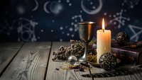 Mystical altar setup with burning candle, ornate chalice, dried herbs and ancient books on wooden table against starry celestial background for spiritual practices.