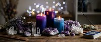 Spiritual meditation setup with colorful candles, amethyst crystals, and healing stones on wooden table with soft bokeh lights creating peaceful atmosphere.