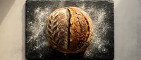 Artisan sourdough loaf with scoring pattern on dark slate board dusted with flour, ready for bakery, culinary, or food photography projects.