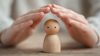 Hands protectively hovering over simple wooden figurine with minimalist features, symbolizing care, protection, and nurturing in mental health or family counseling.