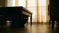 Black cat hiding under wooden coffee table in cozy living room, glowing yellow eyes in shadow, warm curtain light, mysterious mood.
