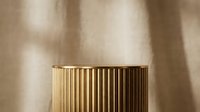 Luxury gold ribbed cylindrical podium on beige linen background with soft shadow overlay for premium product display presentation.