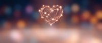 Glowing heart shape made of interconnected light lines floating above blurred bokeh background with warm orange and purple tones for romantic designs.