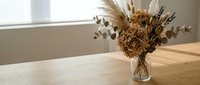 Dried flower arrangement with pampas grass and eucalyptus in glass vase on wooden table near window. Natural home decor for interior design projects.