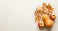 Autumn harvest composition with orange pumpkins, red apples and golden maple leaves on neutral beige background for seasonal decoration and thanksgiving.