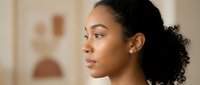 Young African American woman with curly hair in profile view showing natural skincare and wellness lifestyle in warm indoor setting.