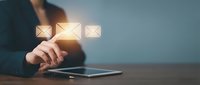 Business professional in dark blazer using tablet to send emails, with glowing envelope icons floating above device on blue background.