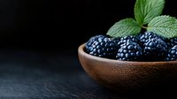 Fresh ripe blackberries in wooden bowl with green leaves on dark background, moody food photography with copy space for healthy eating concept.