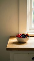 Fresh mixed berries including strawberries, blueberries and blackberries in a wooden bowl on a windowsill with natural sunlight for food and lifestyle content.
