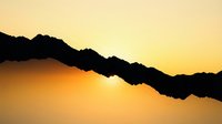 Silhouette of jagged mountain ridge against golden sunset sky with warm orange and yellow gradient light, creating dramatic landscape scenery for nature and travel designs.