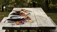 Rustic wooden picnic table with autumn leaves and empty plates outdoors in natural garden setting for seasonal dining and outdoor entertaining.
