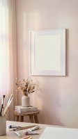 Empty white frame on pink wall with dried flowers and art supplies creating cozy creative workspace for mockup and interior design projects.