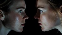 Young caucasian woman facing her mirror reflection in dramatic dark lighting, profile view showing intense emotional expression and introspective mood.