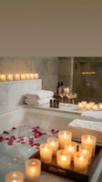 Luxury spa bathroom with candles, rose petals in bathtub, wine glasses and aromatherapy oils creating romantic wellness retreat atmosphere.