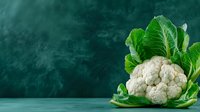Fresh whole cauliflower with green leaves on dark green textured background with copy space. Natural organic vegetables for healthy eating and cooking.