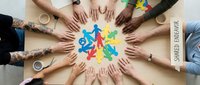 Diverse group of people joining hands in circle around colorful painted handprints, symbolizing unity, teamwork, collaboration, and community support for charitable causes and social initiatives.