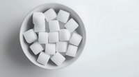 White sugar cubes arranged in ceramic bowl on light background, top view. Clean minimalist food composition for healthy lifestyle and dietary concepts.
