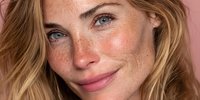 Young blonde woman with freckles and blue eyes smiling naturally, showcasing authentic beauty and confidence for skincare and wellness campaigns.