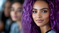 Young African American woman with vibrant purple curly hair and natural makeup smiling confidently at camera, beauty portrait with soft lighting and blurred background.