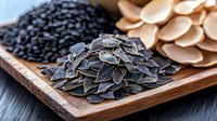 Raw pumpkin seeds, black beans and oyster mushrooms arranged on wooden serving board, macro food photography showing texture and natural ingredients.