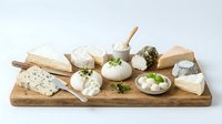 Gourmet cheese platter with assorted artisanal cheeses, crackers and herbs on rustic wooden board for entertaining and culinary presentations.