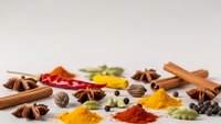 Colorful spices and herbs scattered on white background with cinnamon sticks, star anise, turmeric, paprika, cardamom pods for cooking and seasoning.