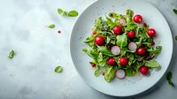 Fresh green salad with cherry tomatoes, sliced radishes and mixed lettuce leaves on white ceramic plate against light background. Healthy eating concept.