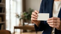Unrecognizable professional woman in navy blazer holding blank white business card in modern office environment with plant decor.