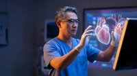 Asian male doctor examining holographic heart model in modern medical facility using advanced technology for cardiovascular diagnosis and treatment planning.