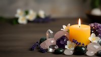 Burning candle surrounded by healing crystals, gemstones and dried lavender on wooden surface creating peaceful meditation and wellness atmosphere.
