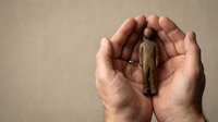 Protective hands cupping small wooden figure symbolizing care, support and human protection in business and personal relationships.