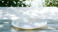 Transparent glass bowl on weathered wooden surface with dappled sunlight and green foliage background, suitable for product photography and design compositions.