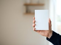 Person holding blank white card or paper in hand, displaying mockup template for branding, marketing, or business communication purposes in modern interior setting.