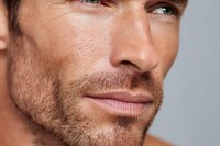 Close up portrait of mature Caucasian male with stubble beard and defined facial features showing confident expression against neutral background.