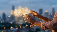 Businessman hands holding glowing digital city hologram with modern skyscrapers against blurred urban skyline at dusk for smart city technology concepts.