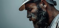 Side profile of mature African American man with gray beard wearing baseball cap, contemplative expression against blurred background, dramatic lighting creates mood.