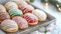 Festive holiday donuts decorated with colorful icing drizzles and sprinkles on metal baking sheet, red and green Christmas theme dessert treats for celebration.