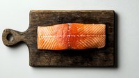 Fresh raw salmon fillet with visible texture on rustic wooden cutting board against neutral background, minimalist food composition for cooking preparation.