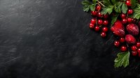 Fresh red currants and ripe pomegranate seeds arranged with green leaves on dark slate background, corner composition with copy space for food design.