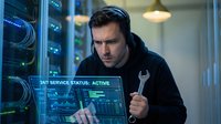 Focused young Caucasian male IT technician with wrench examines holographic server status display in data center, ensuring 24/7 network uptime.