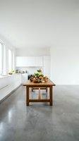Modern minimalist kitchen interior with white cabinets, concrete floors and wooden dining table with fresh vegetables for healthy cooking and meal prep.